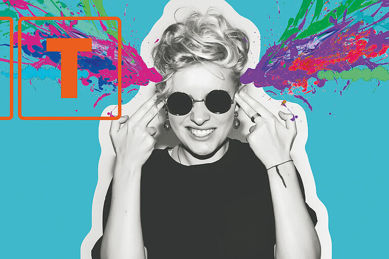 Grafisches Motiv mit den orange umrahmten Buchstaben ‚HIT‘ und der Zahl ‚25‘ auf hellblauem Hintergrund. Rechts eine Person mit Sonnenbrille und schwarzem Shirt, die lachend beide Hände wie Pistolen an den Kopf hält – bunte Farbspritzer in Pink, Grün und Blau explodieren seitlich aus dem Kopfbereich.